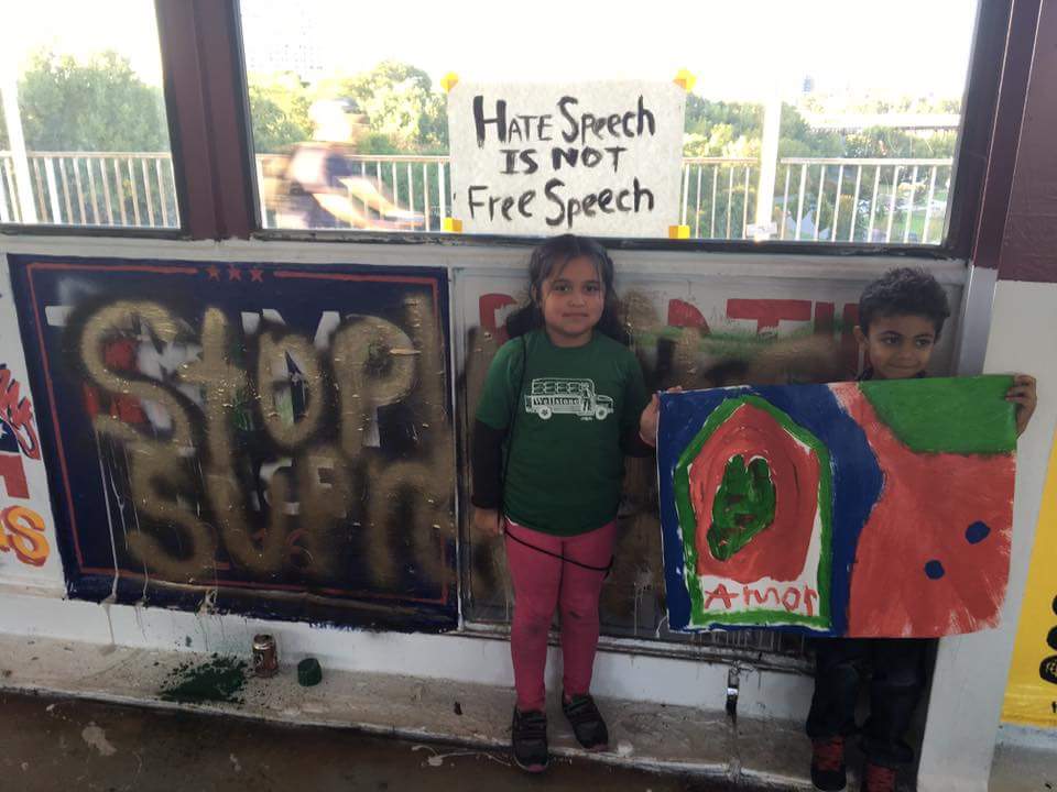 Children in front of the mural. A sign behind reads "Hate Speech is not Free Speech."